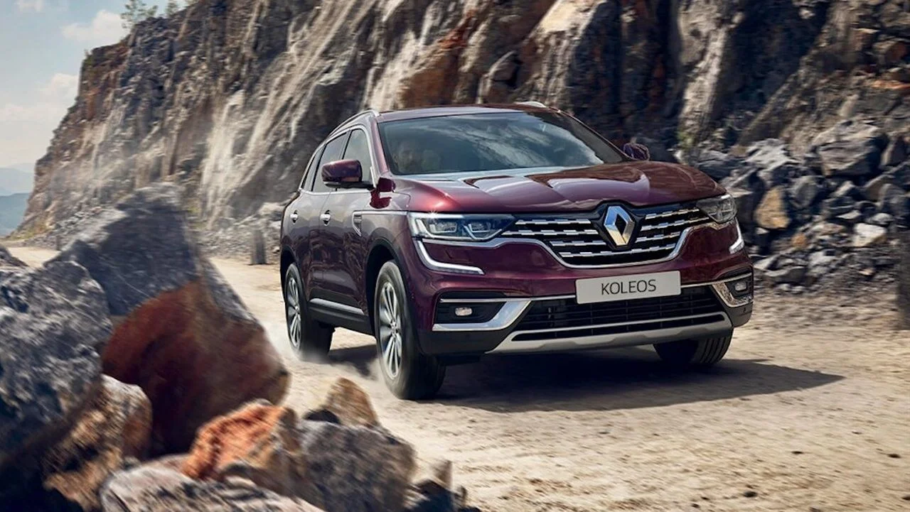 Бордовый Renault Koleos второго поколения после рестайлинга едет по каменистой дороге